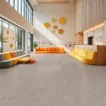 Bright modern lobby with orange and yellow seating, large windows, and a gray carpeted floor