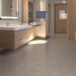 Empty modern restroom with beige tile floors, a long sink counter, and a wall-mounted TV near the doorway