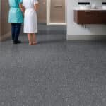 Two people walking on a gray carpet in a modern hallway, with a reception desk on the right.