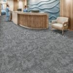 Modern lobby with curved wooden reception desk, gray patterned carpet, and beige chairs.