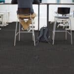 Person sitting at a desk in an office, with a chair and backpack on the floor nearby.