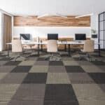 Modern office with three desks, computers, and beige chairs on a checkered carpet.