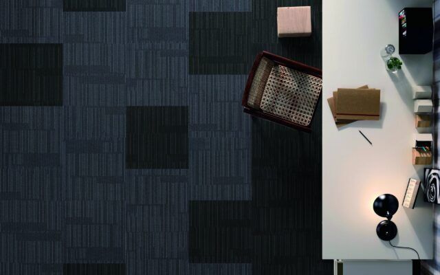 Top-down view of a desk with a lamp, plant, notebook, and keyboard beside a dark patterned carpet.