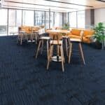 Modern lounge with wooden high tables and stools on a dark blue carpet in a bright, glass-walled room