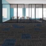 Empty office room with glass walls, blue chairs, and patterned carpet near large windows