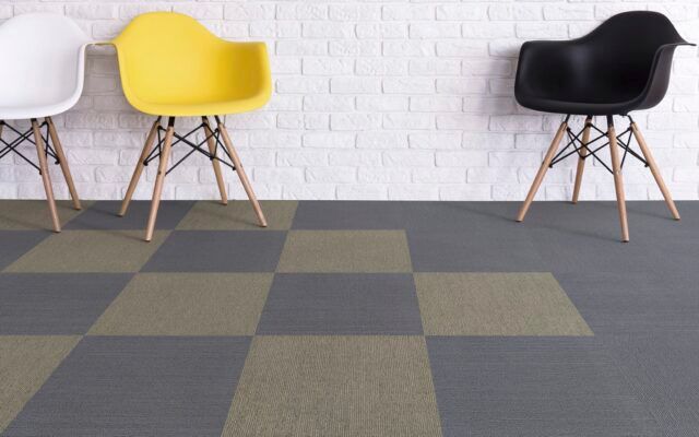 Modern lounge with white, yellow, and black chairs on a gray checkered carpet against a white brick wall