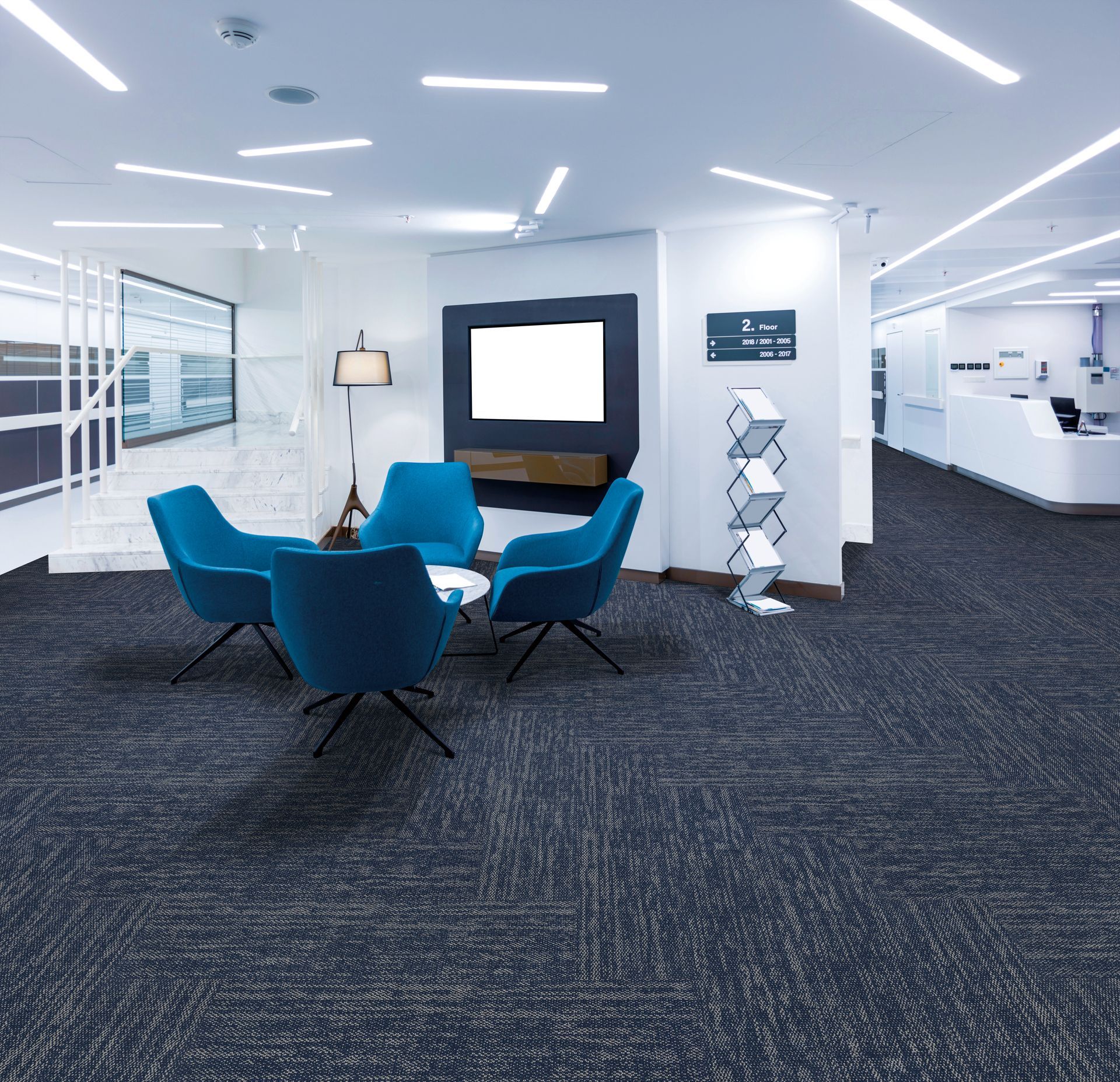 Modern office lounge with blue chairs, a round table, and carpeted open workspace behind it