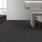 Empty modern room with gray carpet, white walls, and a small seating area by a window.