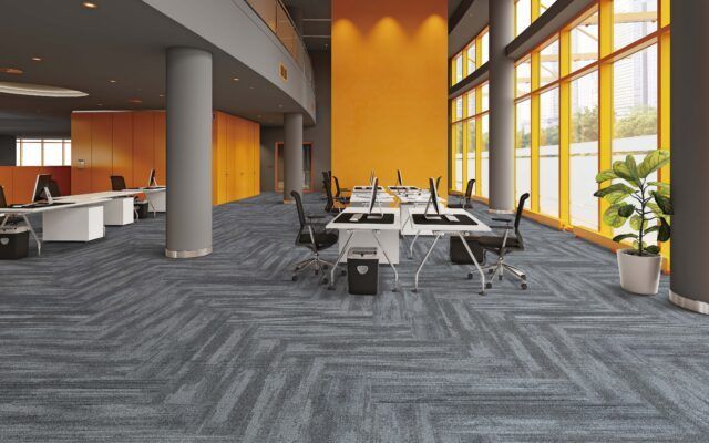 Modern office lounge with gray carpet, orange walls, tables, chairs, and large windows with plants