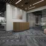 Modern office lobby with curved wood reception desk, gray patterned floor, and exposed ceiling beams.