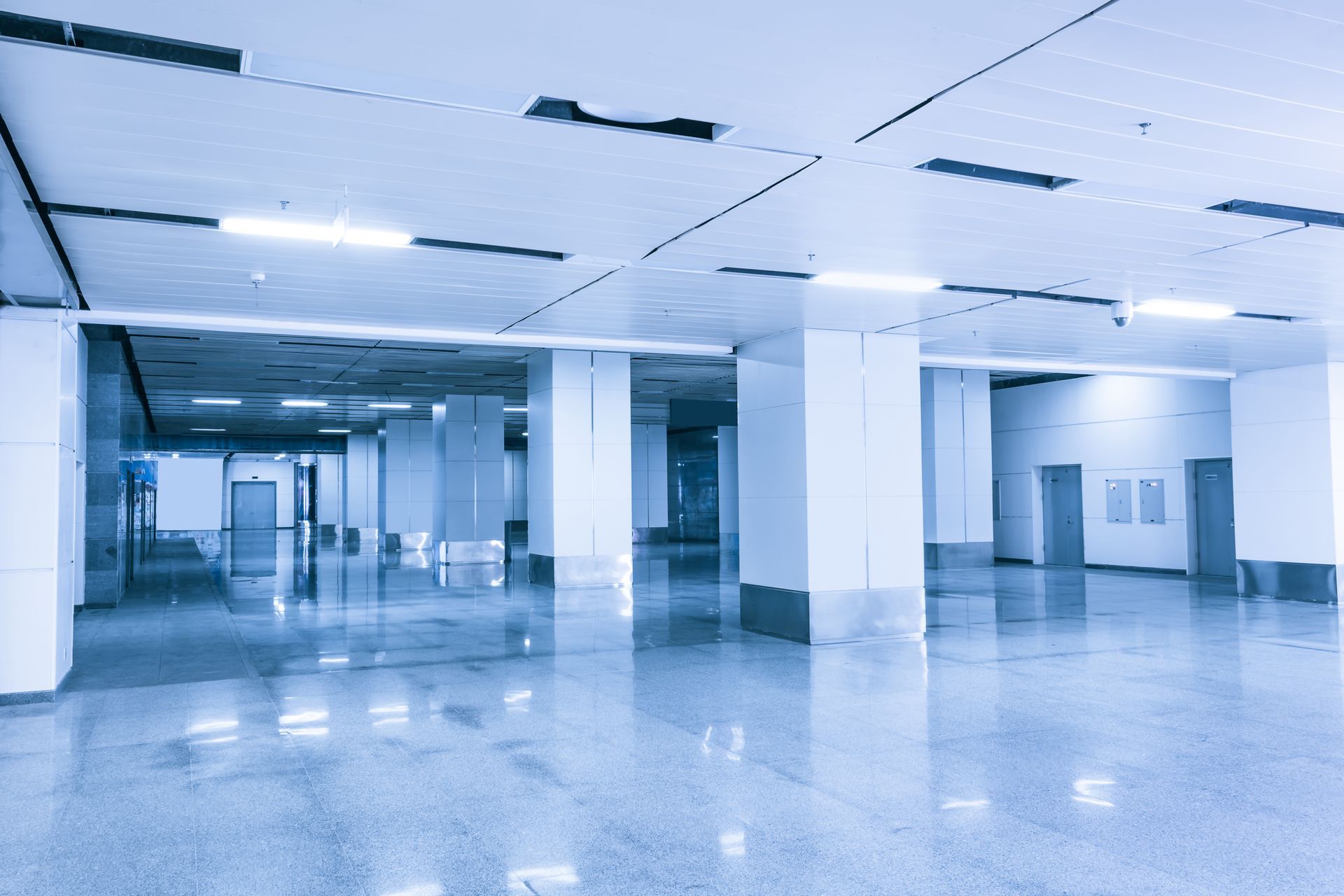 Empty modern office lobby with blue-tinted lighting, white columns, and polished floor