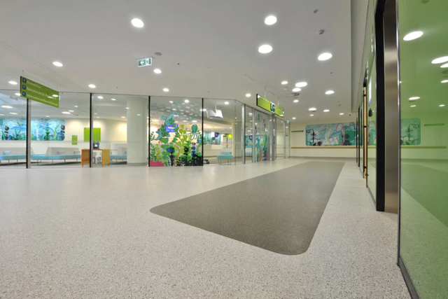 Bright modern lobby with glass walls, white ceiling lights, and a gray carpeted path