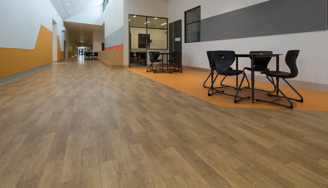 Empty hallway with wood-pattern floor, orange walls, and a small seating area with black chairs and tables