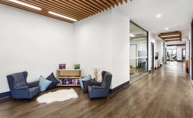 Modern office lobby with blue lounge chairs, wooden floor, and hallway view