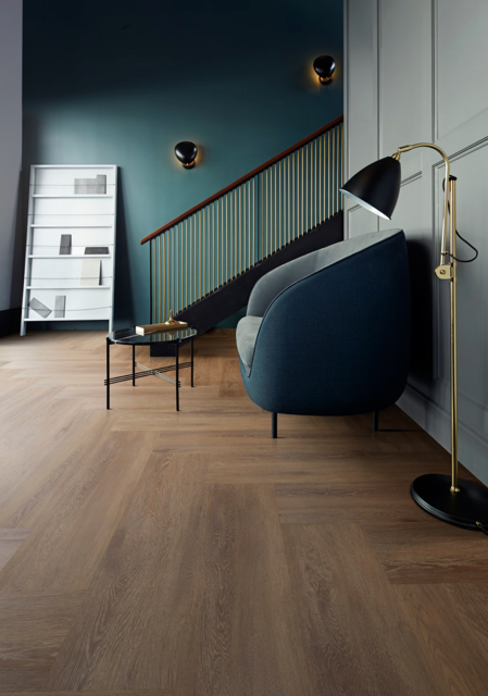 Modern living room with blue chair, brass lamp, staircase, and wood floor