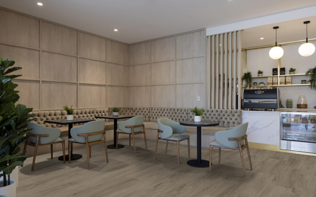 Modern café interior with pastel chairs, round tables, wood-paneled walls, and hanging globe lights