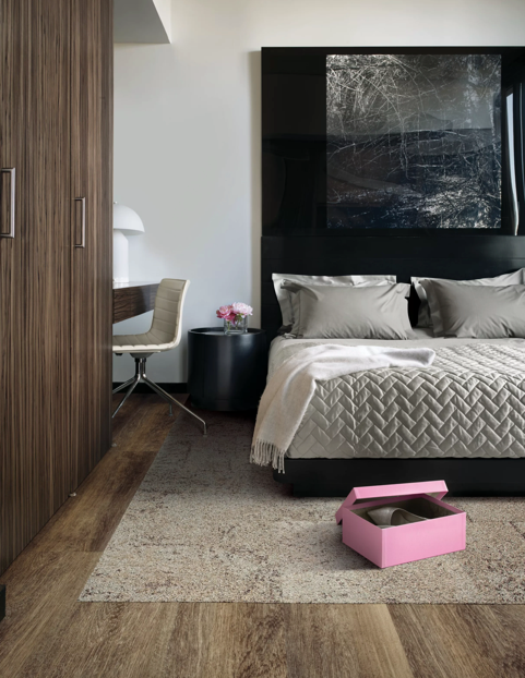 Modern bedroom with a bed, wood wardrobe, desk chair, and a pink box on the rug.