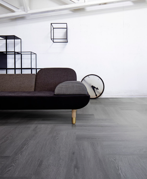 Modern living room with a dark sofa, gray flooring, white wall, and minimalist shelves.