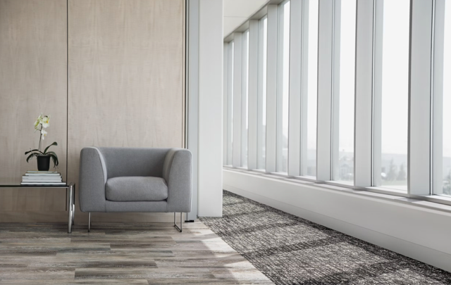 Minimalist office lounge with a gray armchair beside a small side table and large windows overlooking a city view