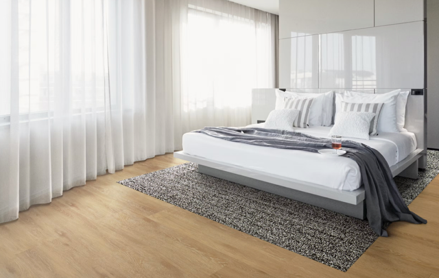 Bright modern bedroom with a neatly made bed, gray rug, and sheer curtains by large windows