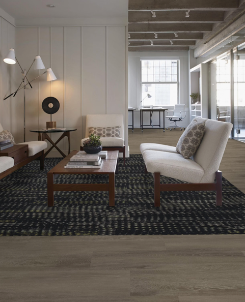 Bright modern living room with white sofas, patterned rug, wood coffee table, and large windows