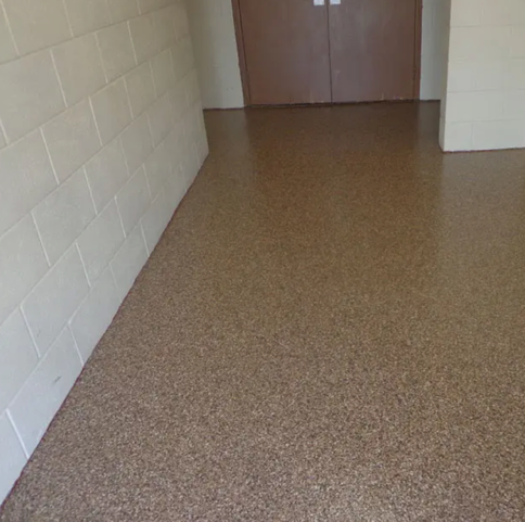 Empty hallway with brown speckled floor and white block walls leading to closed double doors.