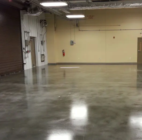 Empty warehouse with polished concrete floor, beige walls, a brown roll-up door, and overhead lights.