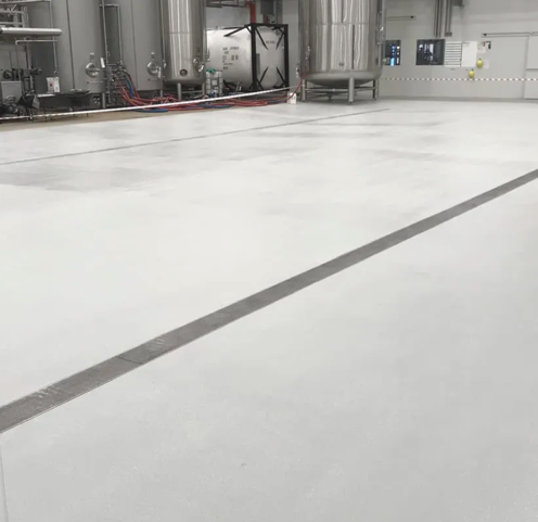 Empty industrial room with a smooth white floor, gray wall, pipes, and equipment in the background