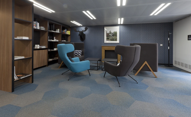 Modern office lounge with blue and brown chairs, bookshelves, desks, and a framed wall print