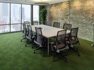 A modern boardroom with a white table and mesh office chairs, set against a brick wall with floor-to-ceiling windows.