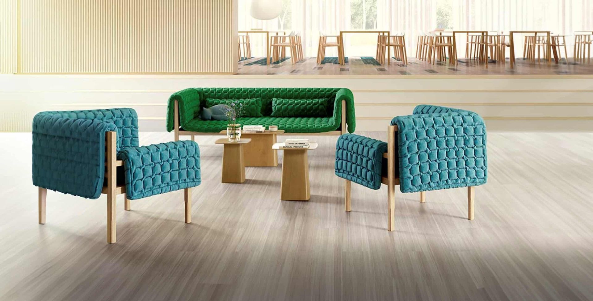 A green sofa and two teal armchairs with textured fabric and light wood legs arranged around small tables in a bright room.