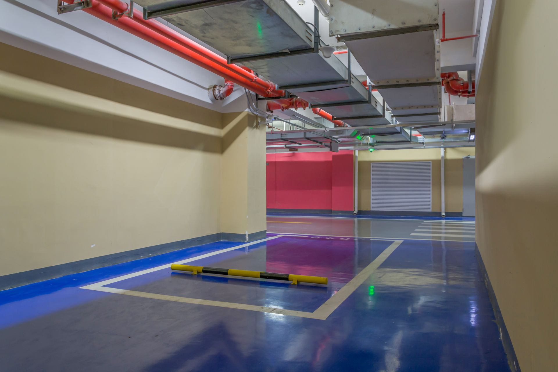 An empty parking space with blue floor markings and a yellow bumper in a modern underground parking garage.