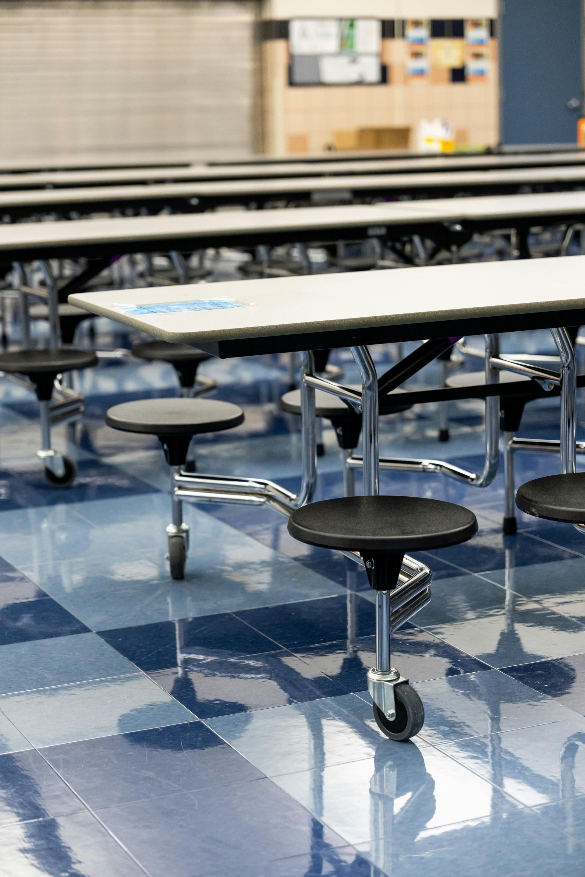 Rows of cafeteria tables with attached swivel seats on a blue and white checkered floor.