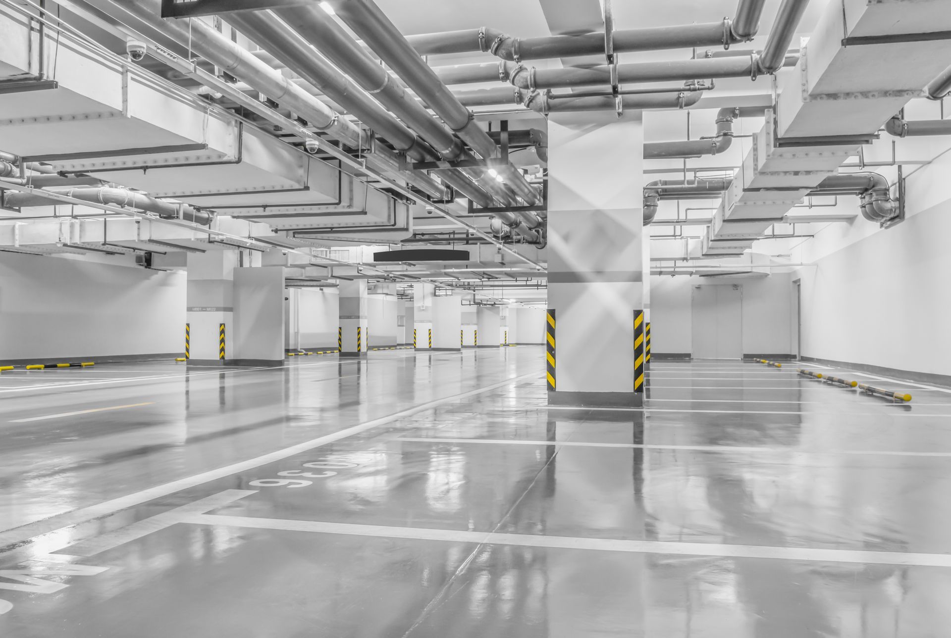 Empty underground parking garage with glossy concrete floor, white walls, and exposed ceiling pipes