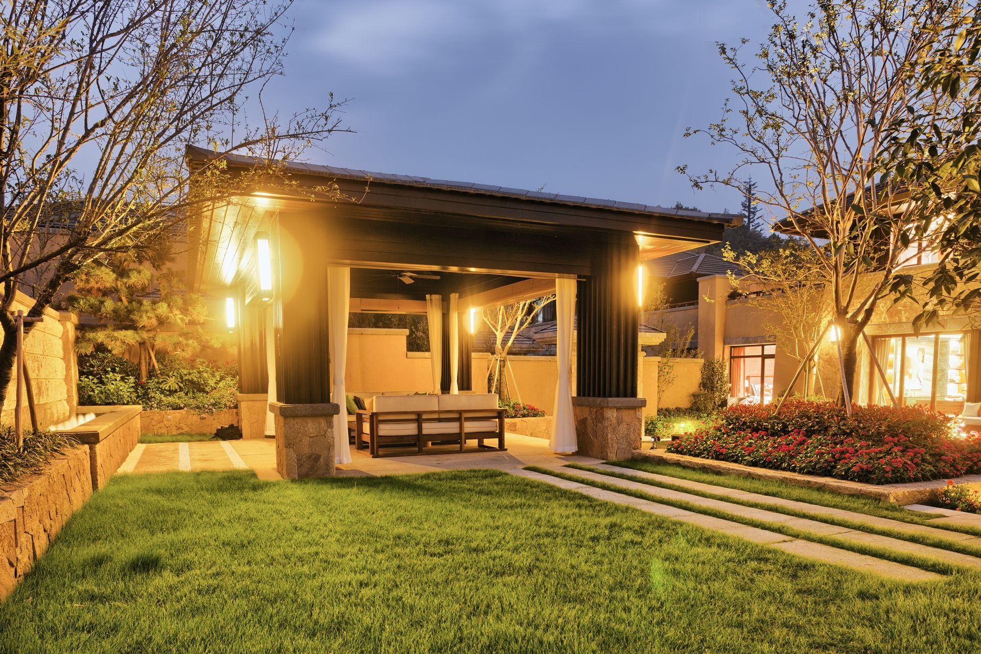 Warmly lit modern home porch with a grassy yard and stone steps at dusk