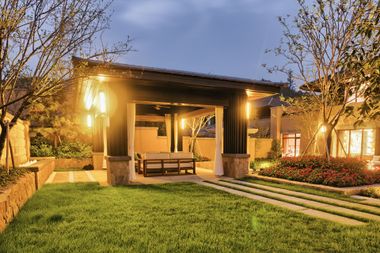 Warmly lit modern house patio and lawn at dusk, with a bench, steps, and garden landscaping.