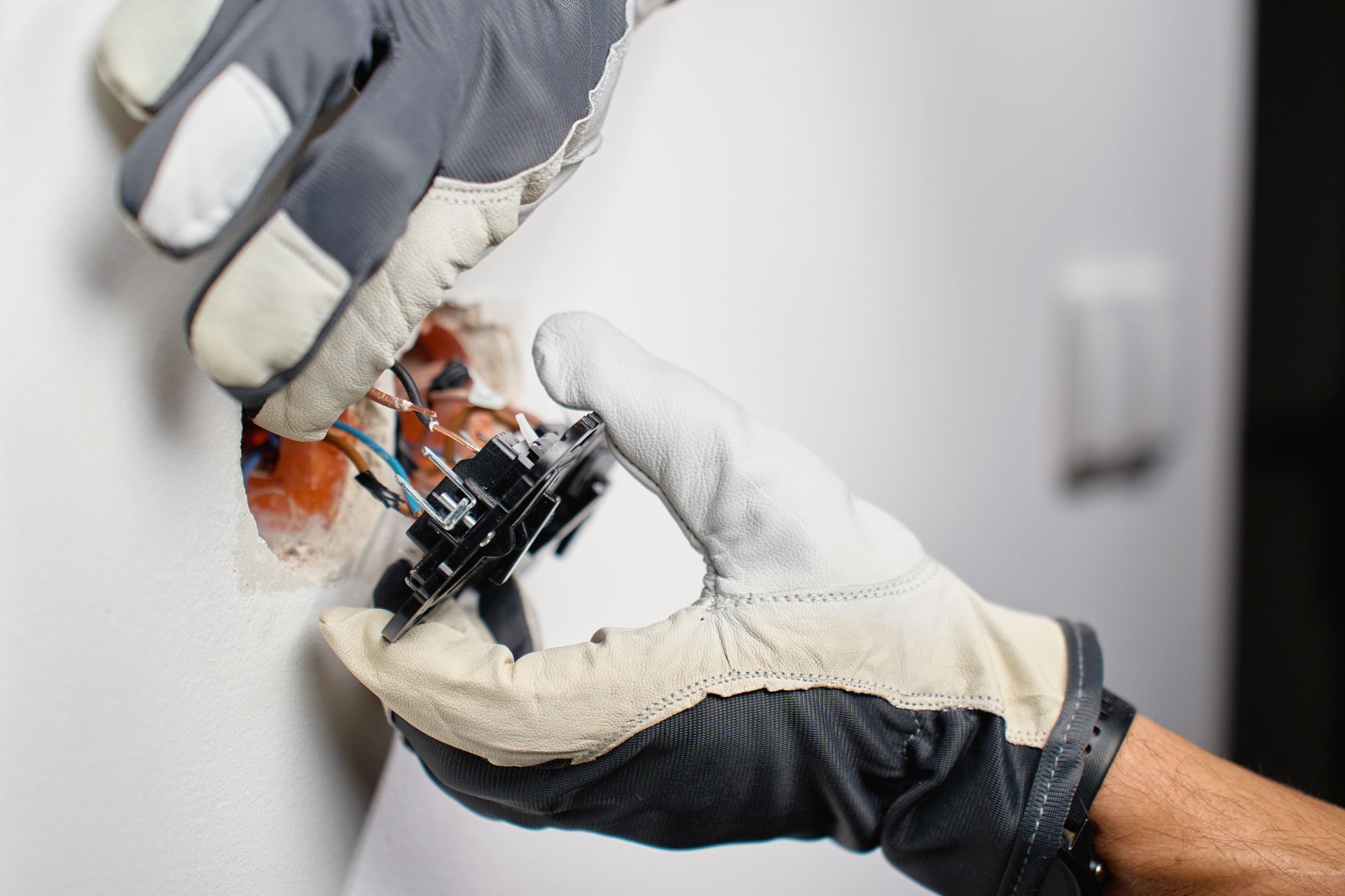 Gloved hands handling a small black device over an open electrical component