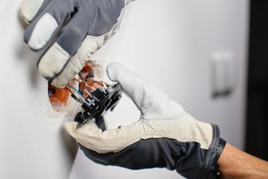 Gloved hands handling a small black device over an open electrical component