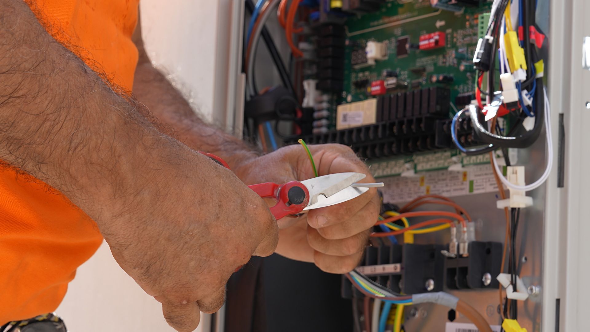 Technician wiring an electrical panel with tools and exposed cables