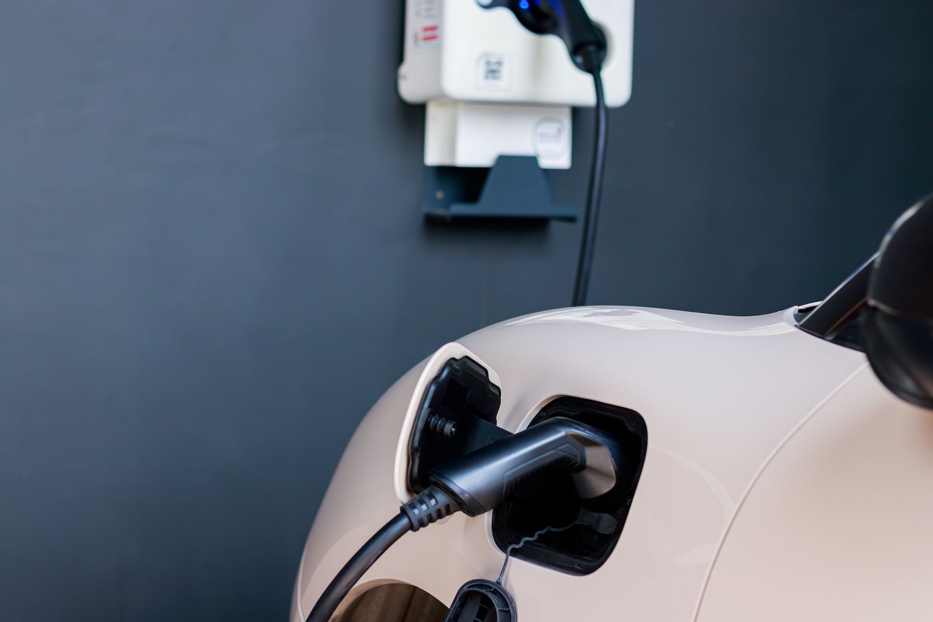 Electric vehicle charging plug connected to a white car at a wall charger in a dark garage