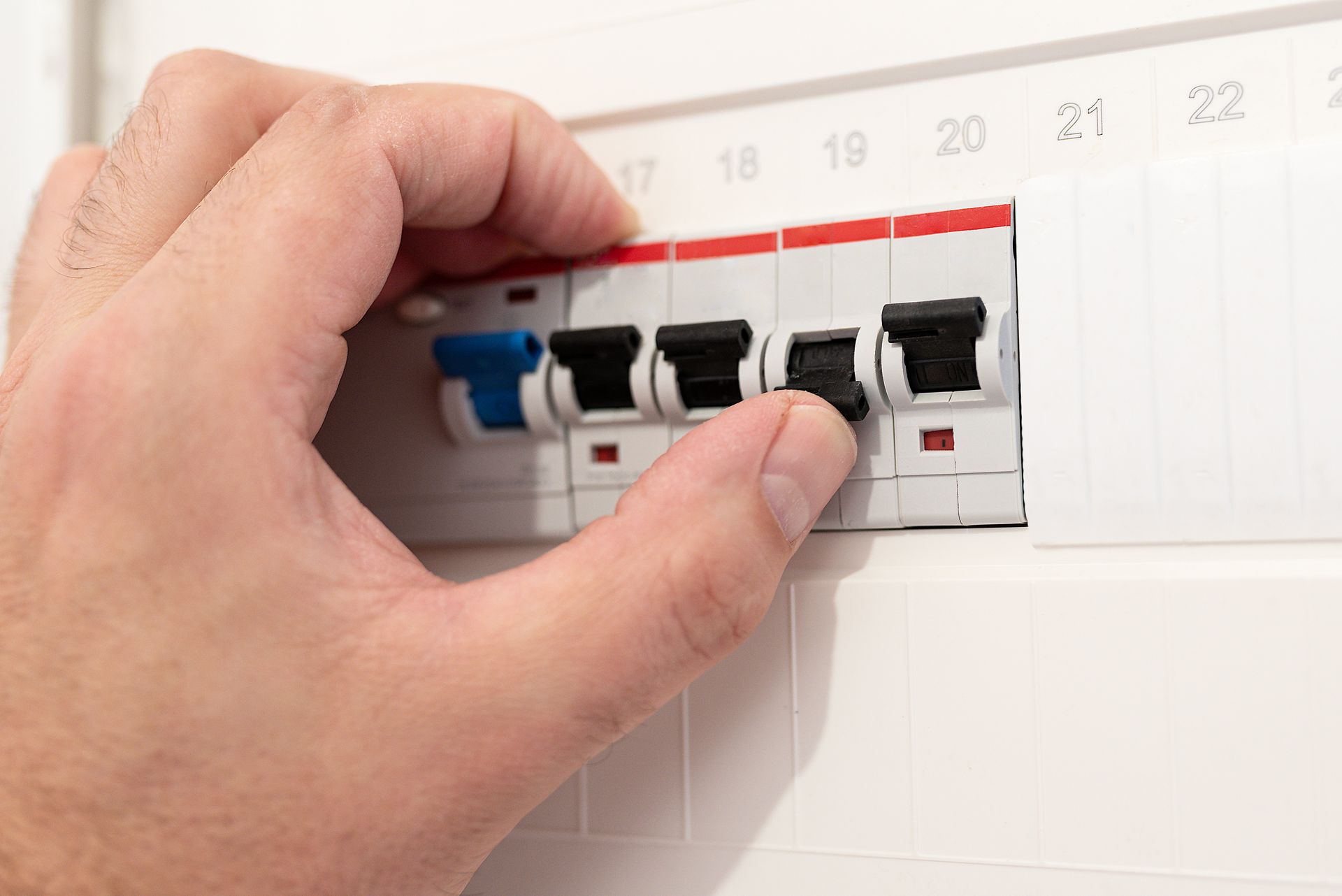Hand turning off a row of electrical circuit breakers on a white panel