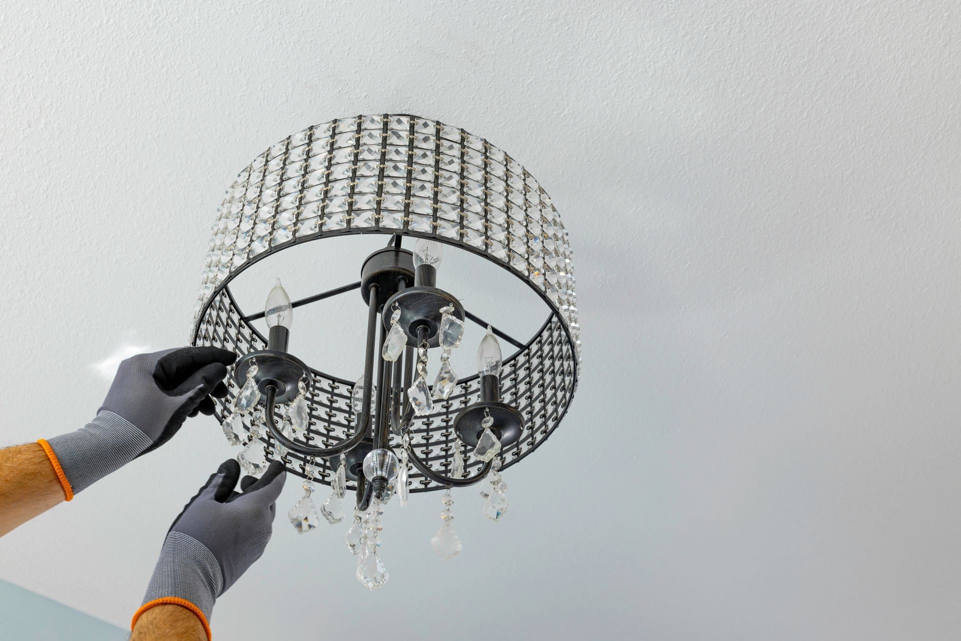 Gloved hands adjusting a modern chandelier with crystal strands against a white ceiling