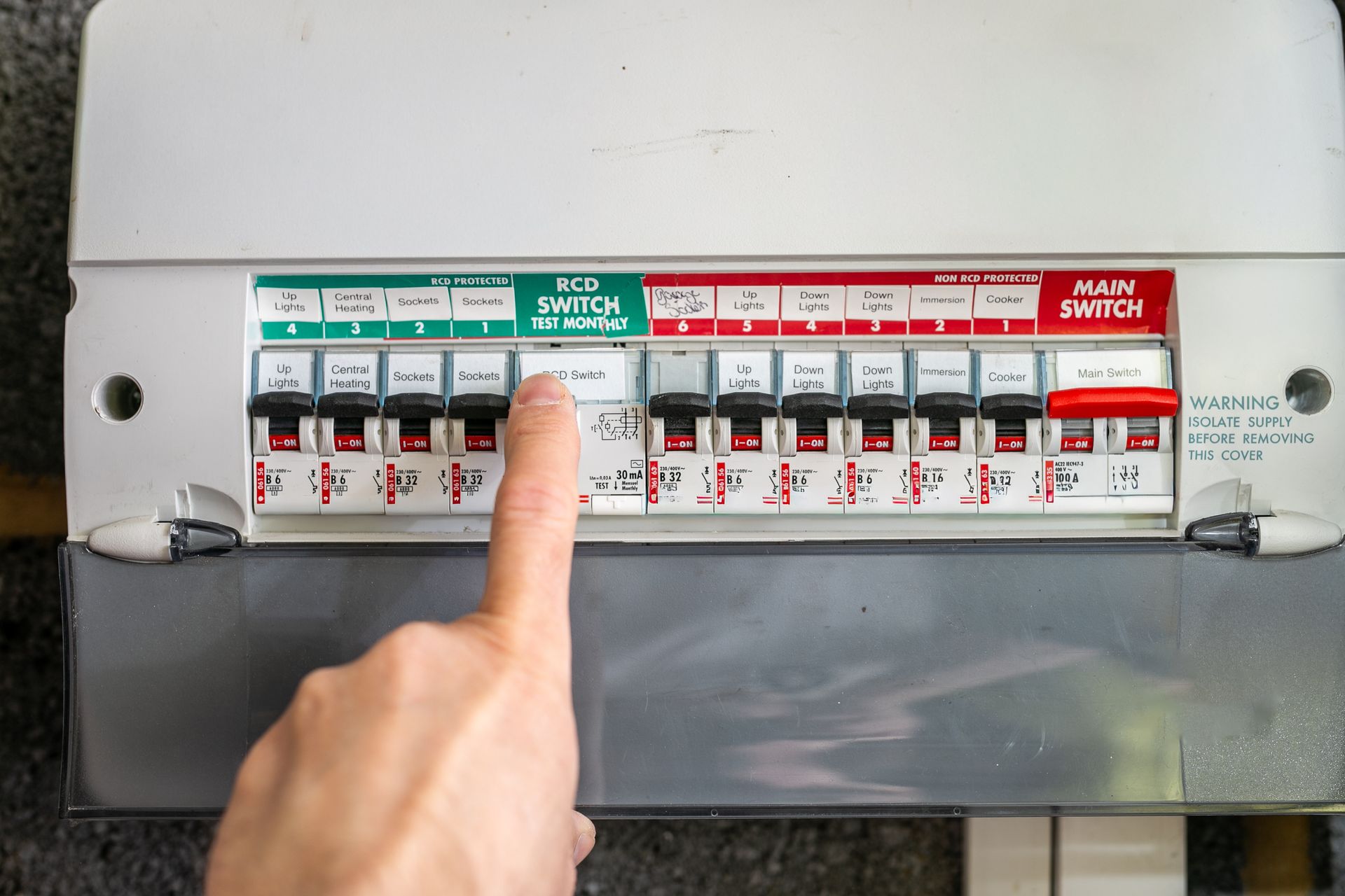 Finger pointing to a row of circuit breakers in an electrical panel with red and green switches