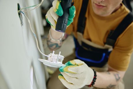 Technician in gloves installing an electrical outlet on a wall with a screwdriver