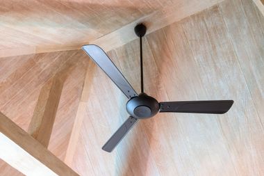 Ceiling fan with three dark blades on a textured tan ceiling