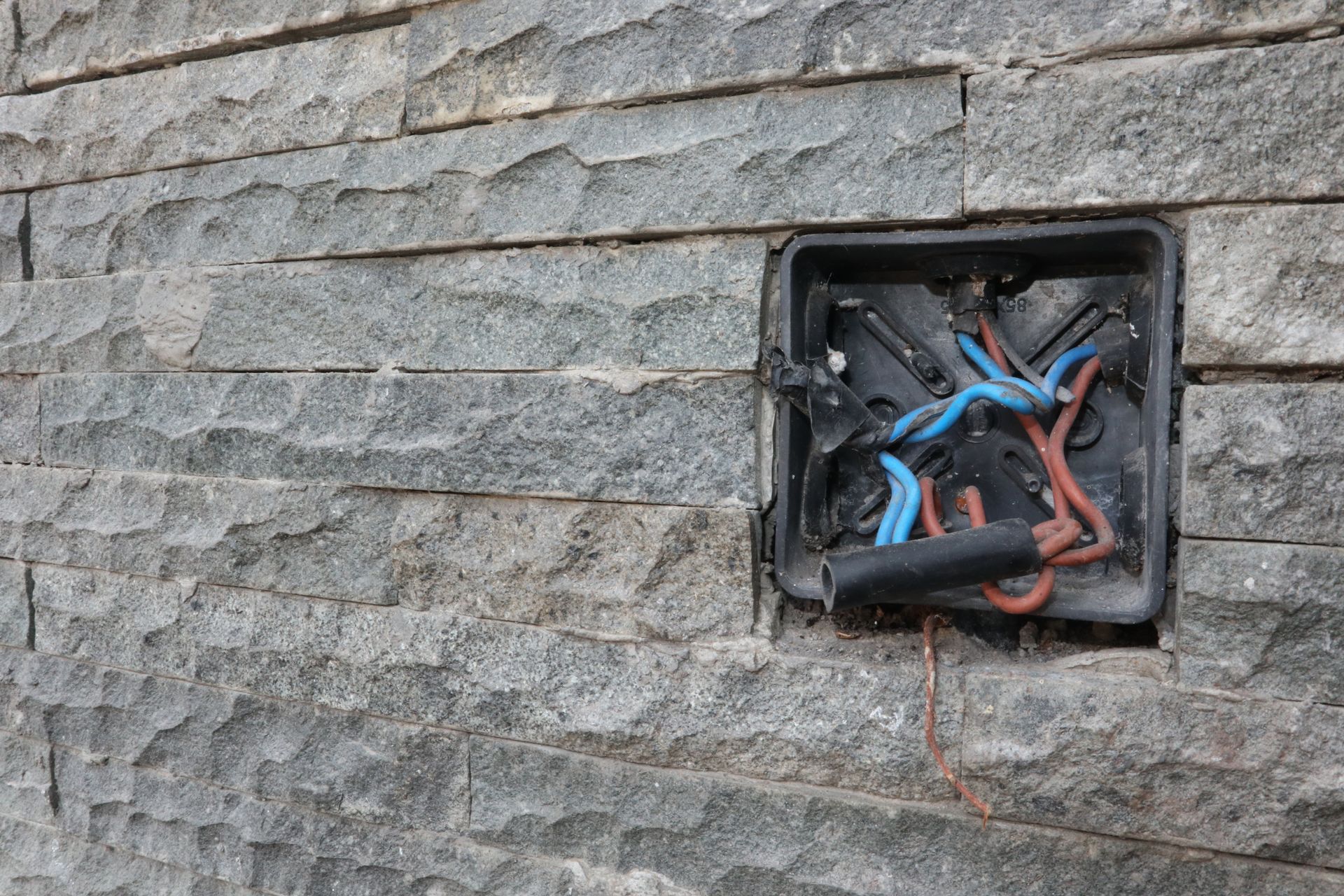 Exposed electrical wires in a wall-mounted junction box on a stone exterior wall