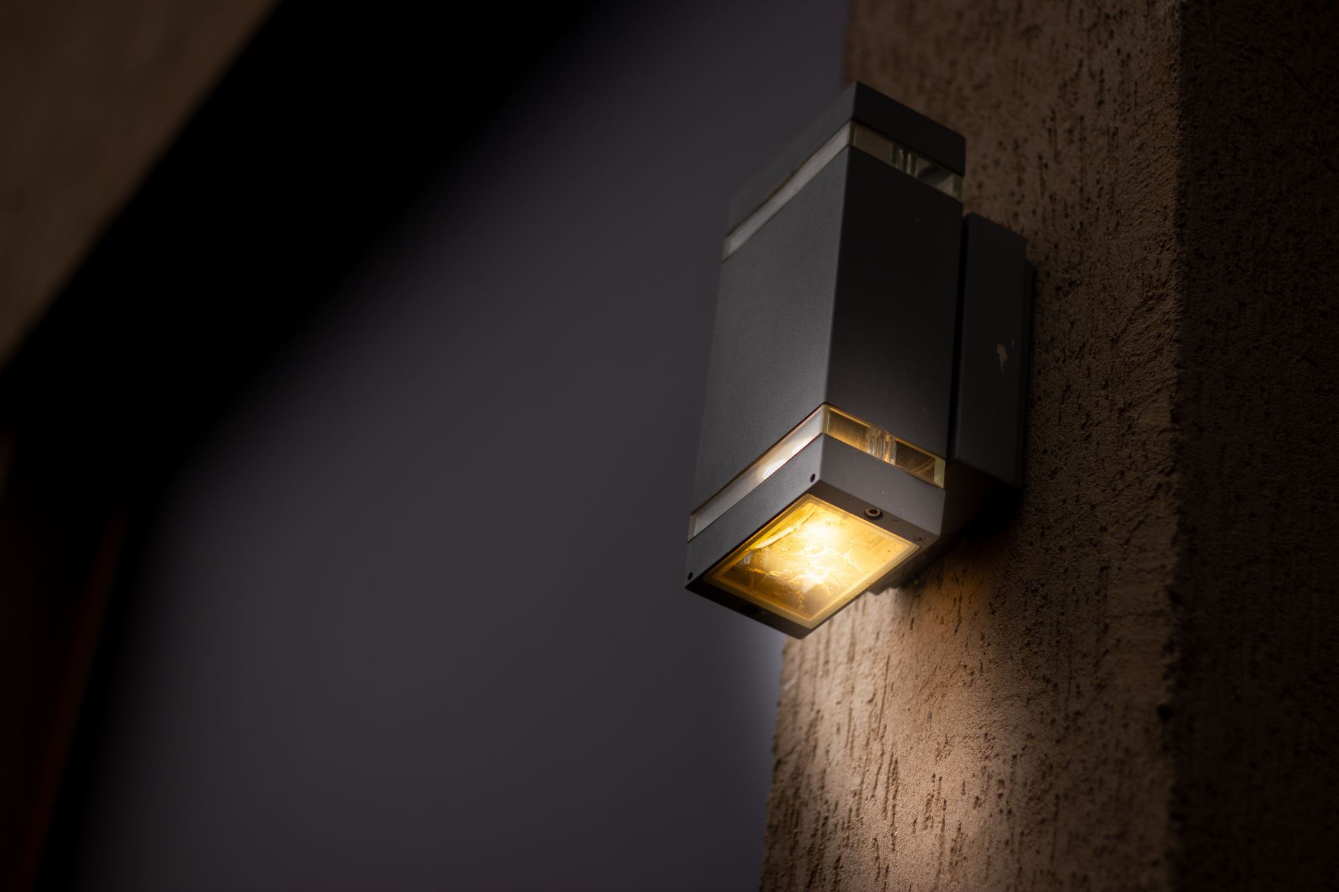Modern wall sconce with warm light on a textured exterior wall at night