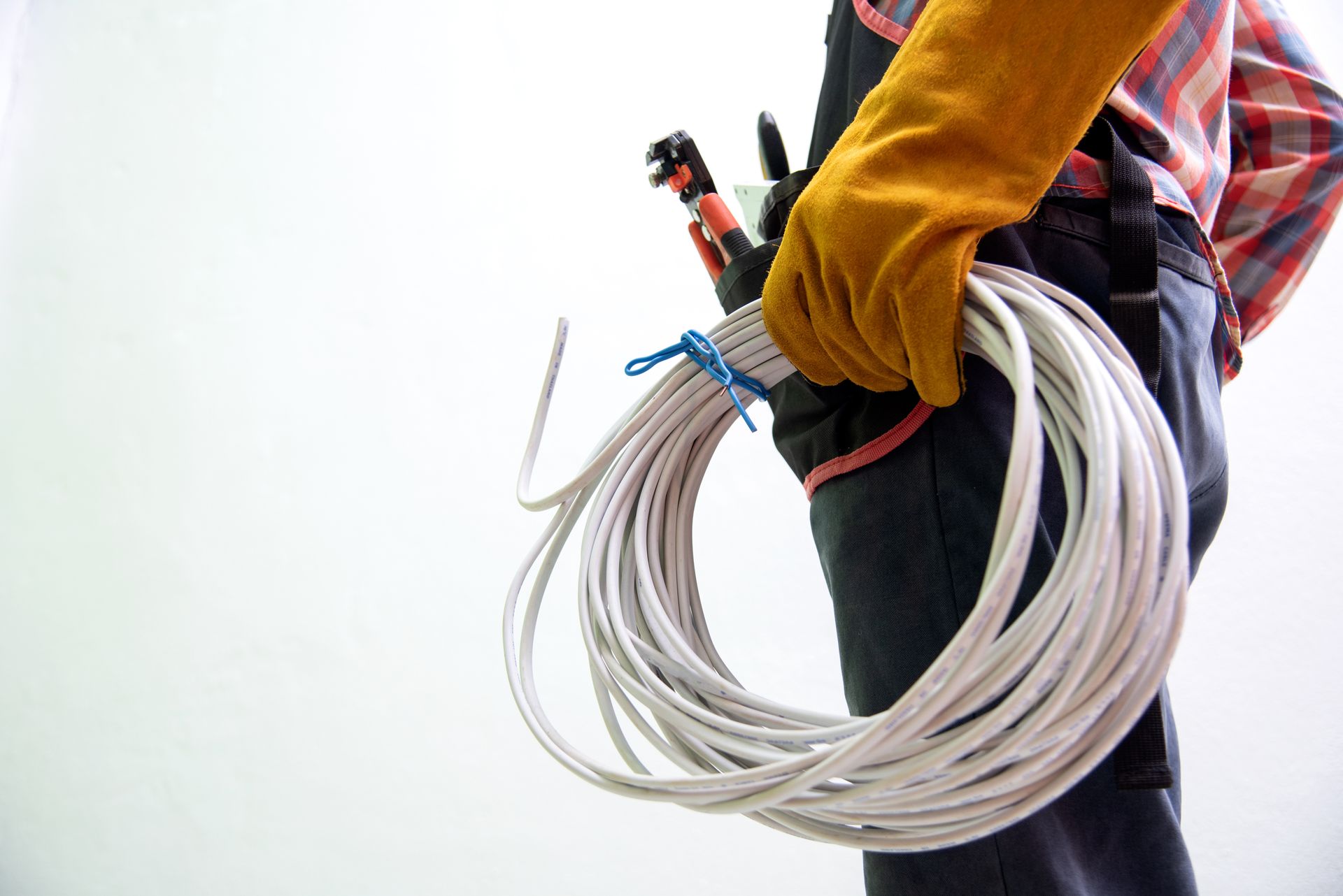 Worker in orange gloves carrying a coiled white cable on a rooftop