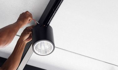Hands installing a black ceiling track light on a white ceiling