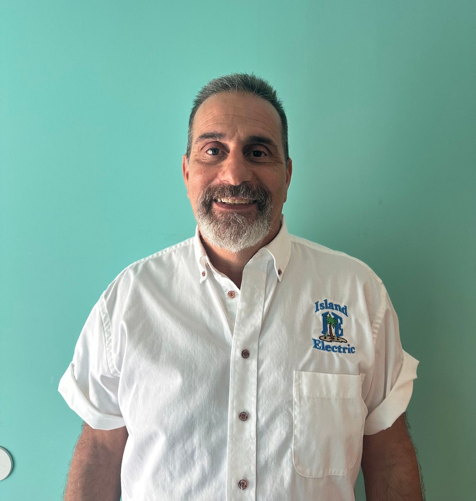 Smiling man in a white short-sleeve button-up shirt against a teal wall